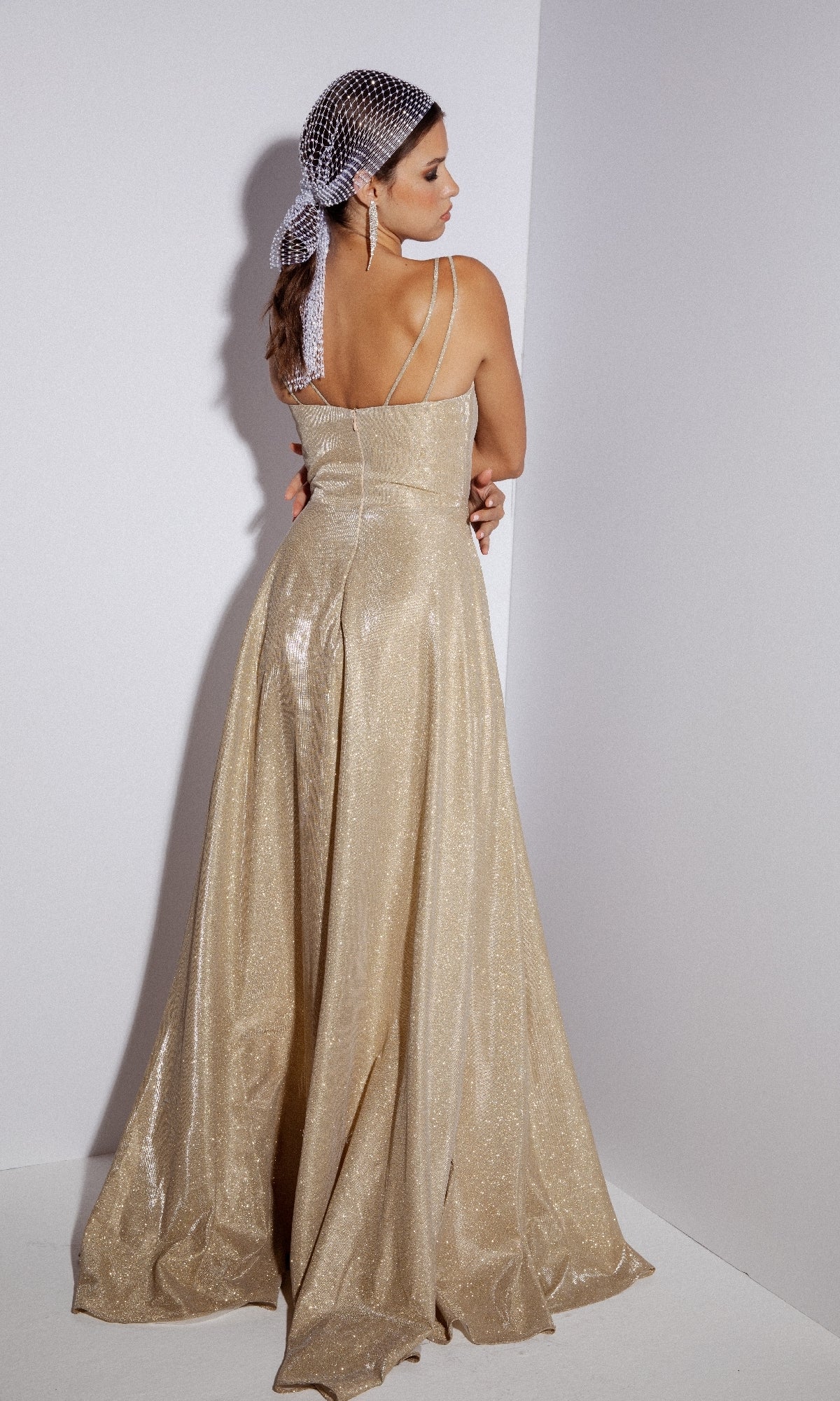 A woman in the Eureka 8900 Sleeveless Long Glitter Formal Dress faces the corner, paired with a beaded headscarf and long earrings.